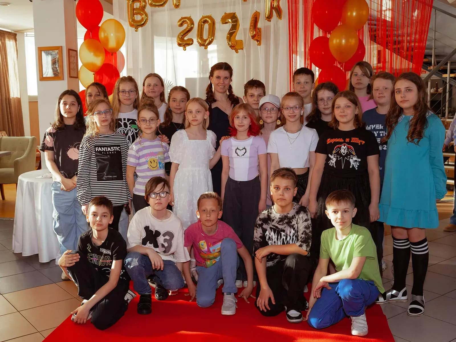 Выпускники начальной школы с учительницей у стены с золотыми шарами «Выпуск 2024»